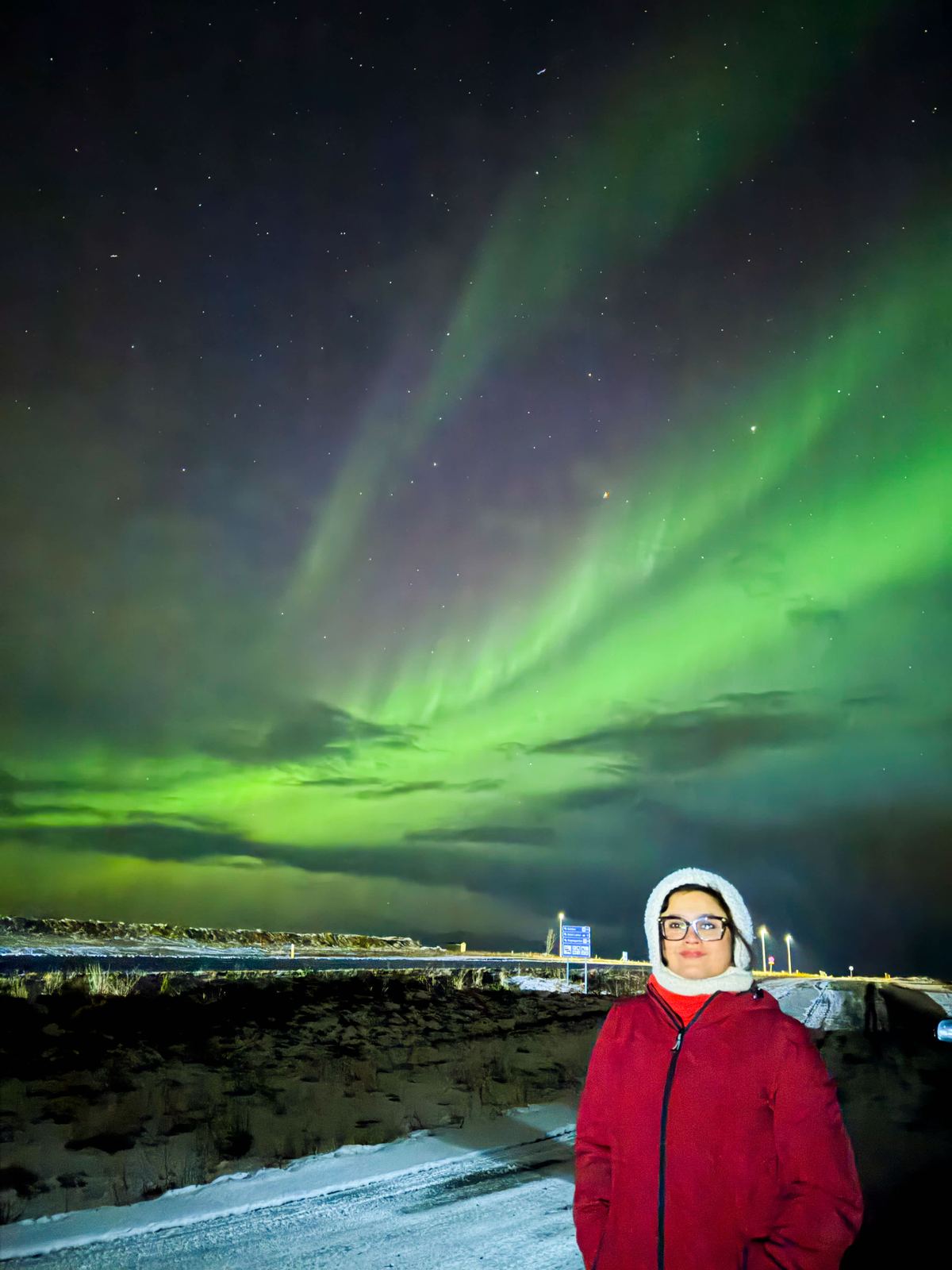 Northern lights solo — green and magenta aurora filling the sky, person in red jacket below
