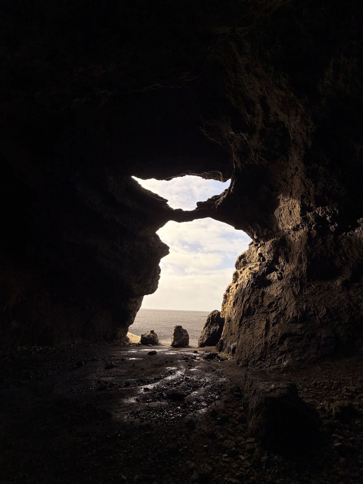 Yoga cave — dark cave, two natural rock openings framing the sea and rocks